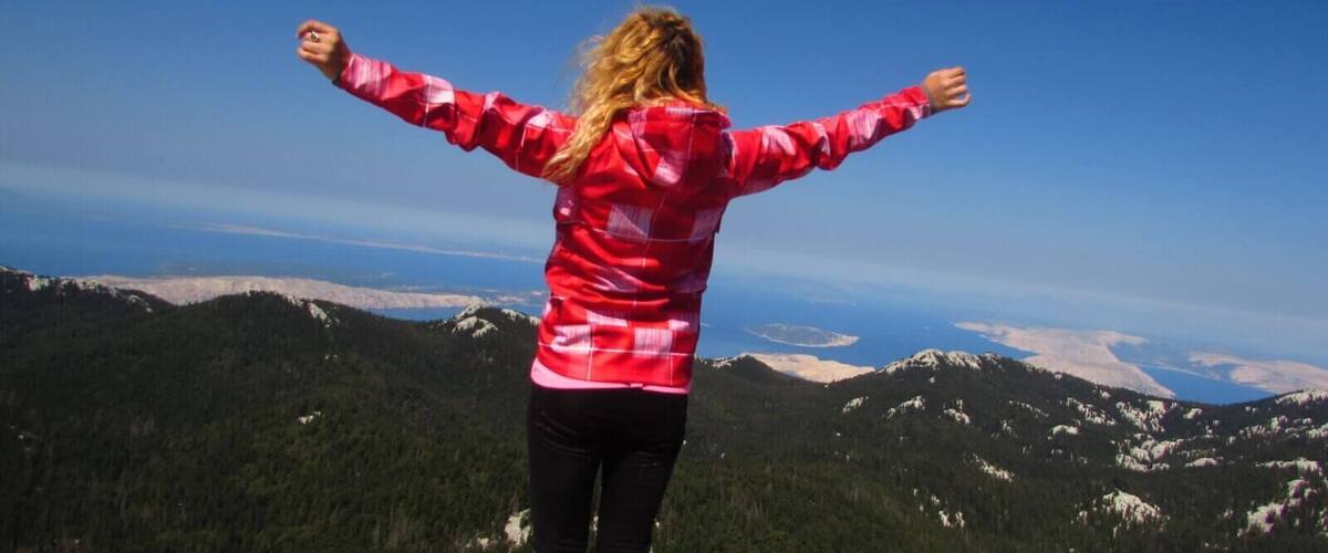 A person standing on a rock with arms outstretched, overlooking a mountainous landscape.