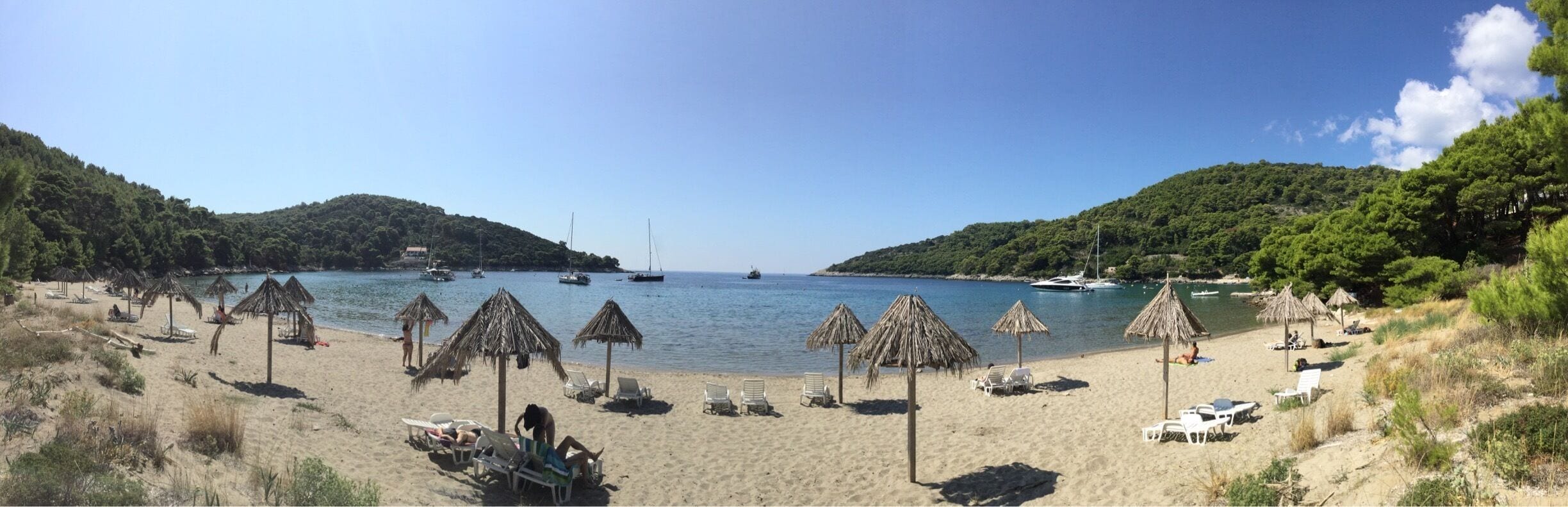 A beach with thatched umbrellas, lounge chairs, and boats on the water.
