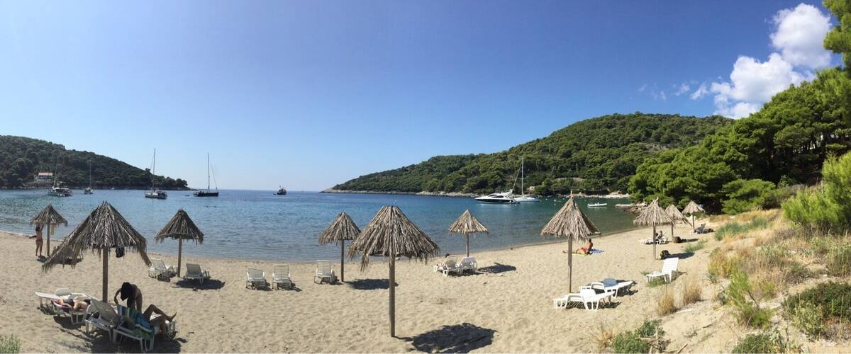 A beach with thatched umbrellas, lounge chairs, and boats on the water.