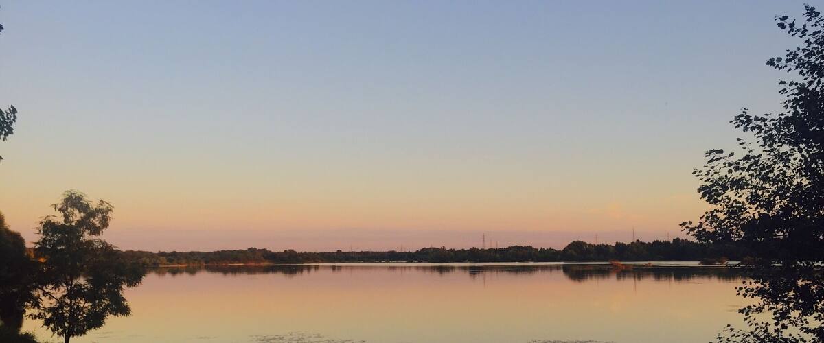 A calm lake at sunset with trees on the banks and a clear sky.