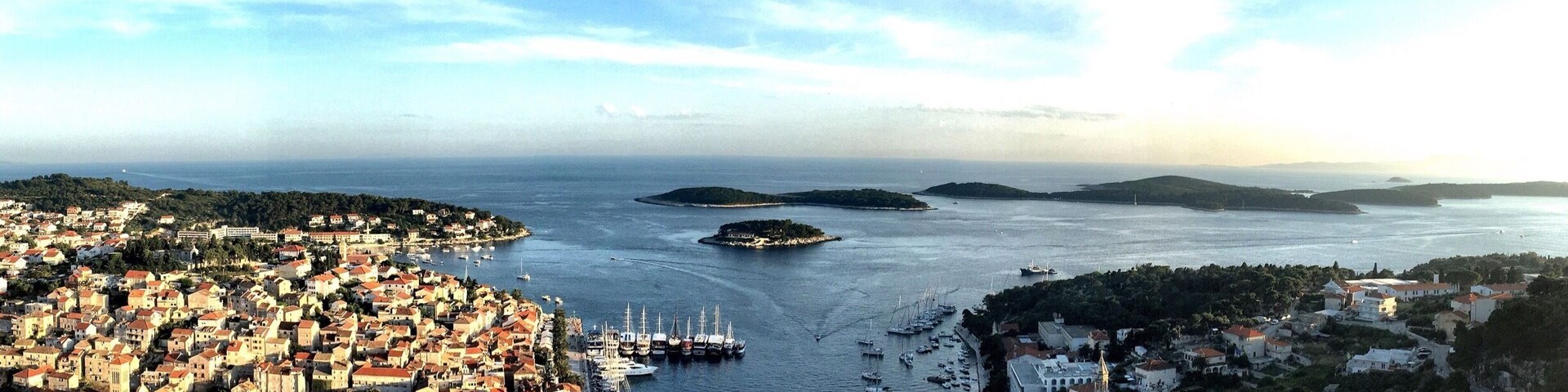 A coastal town with a historic fort, a harbor with boats, and a clear view of the sea and distant islands.