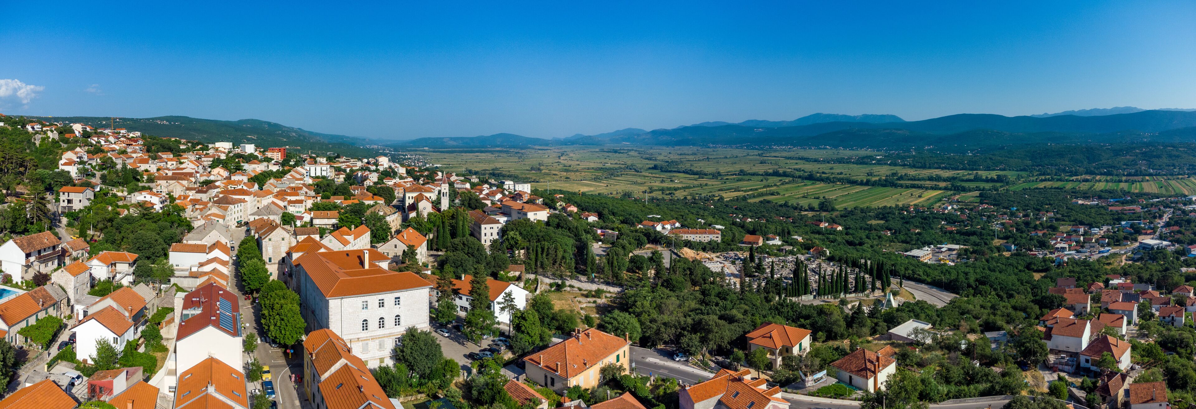 A town with red-roofed buildings, a prominent church, and rolling hills in the background.