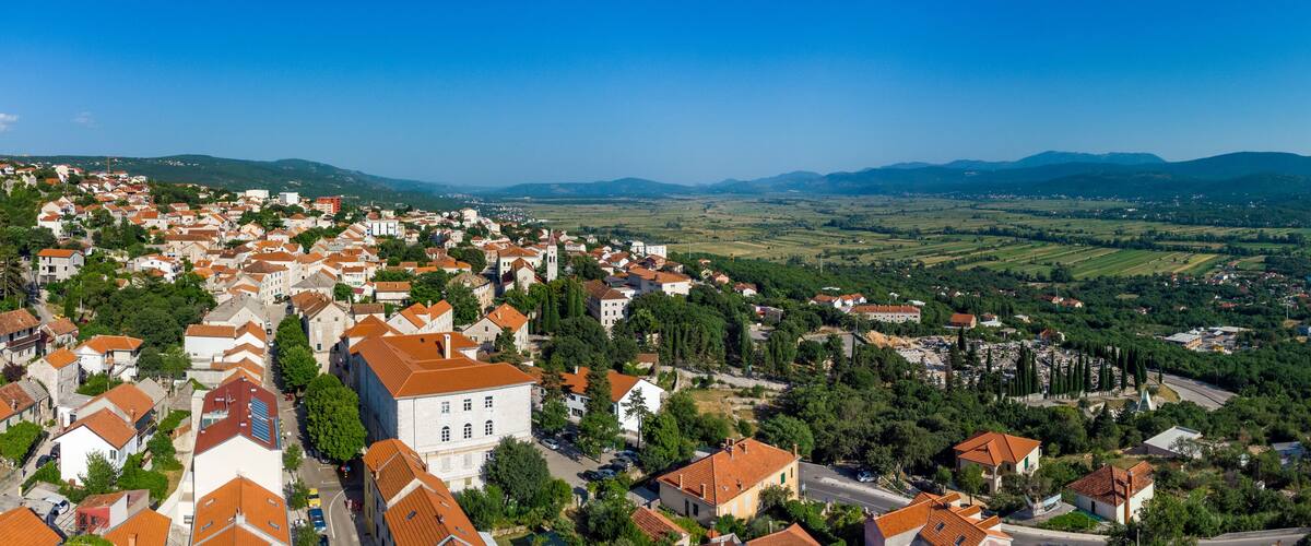 A town with red-roofed buildings, a prominent church, and rolling hills in the background.