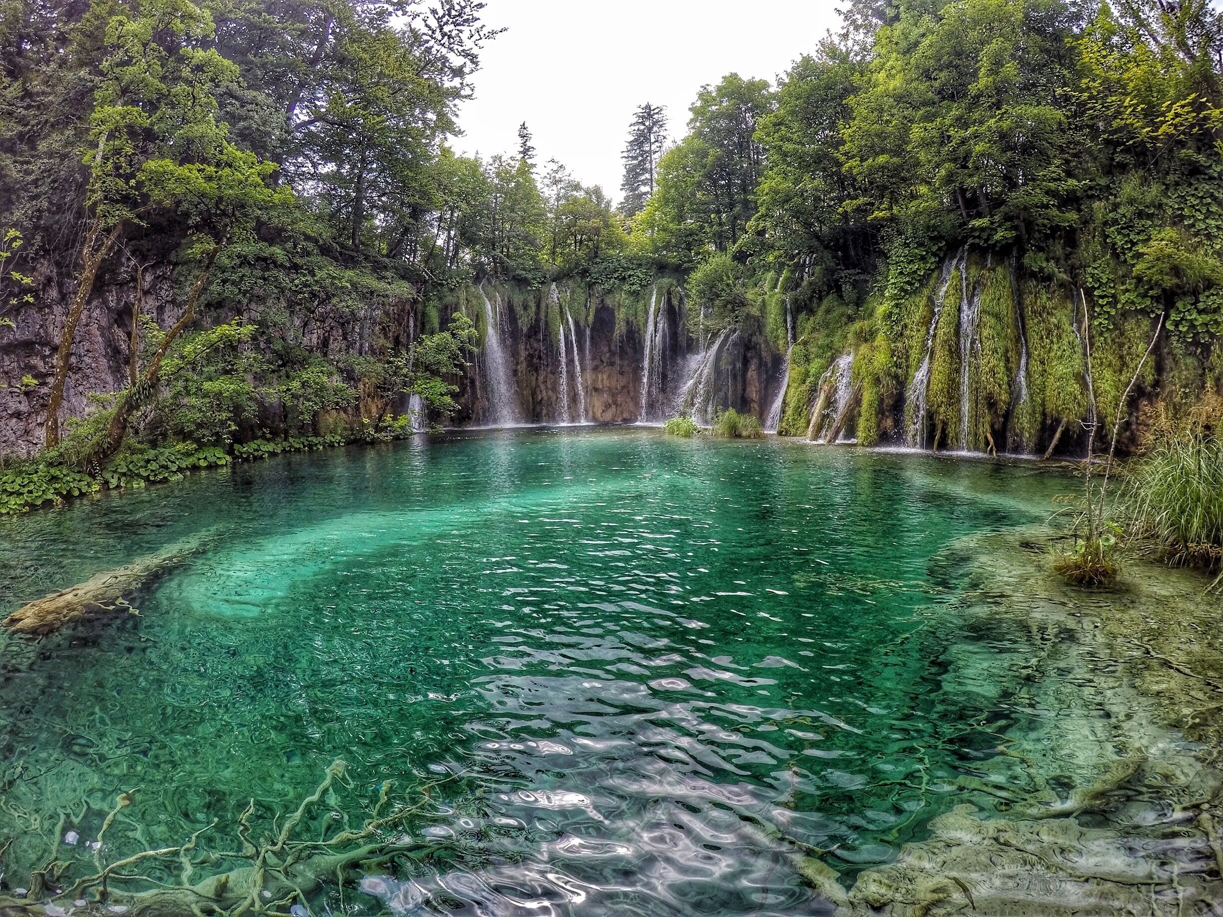 A clear, turquoise lake surrounded by lush greenery and cascading waterfalls.