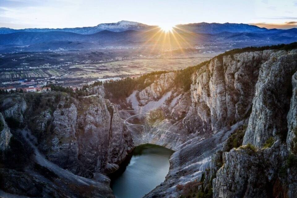 Ein Tal mit einem See, umgeben von Felsen und Bergen im Hintergrund.