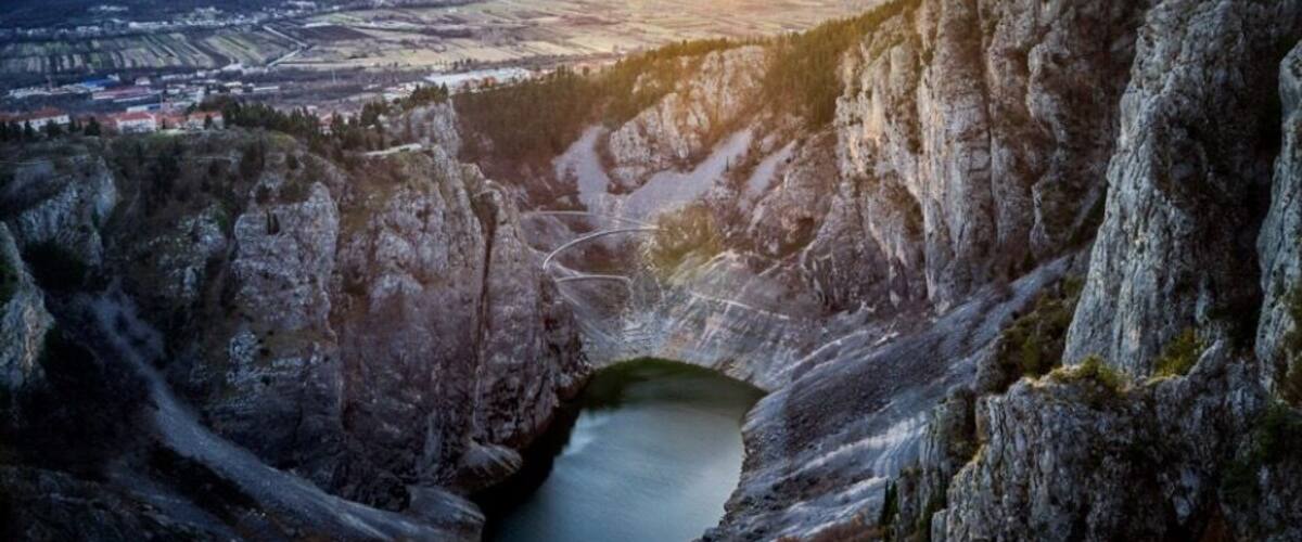 A valley with a lake surrounded by cliffs and mountains in the background.