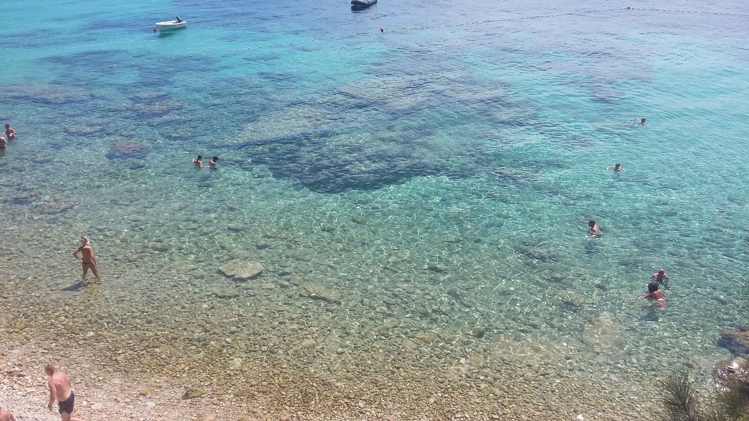 A clear beach with people swimming and standing in shallow water.
