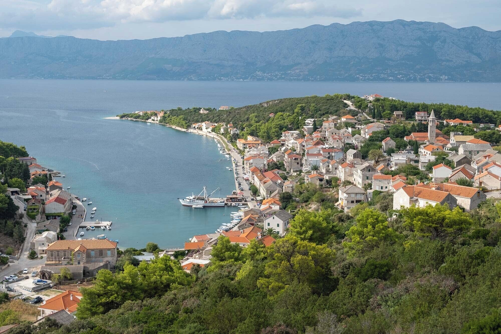 A coastal town with a marina, surrounded by hills and a clear view of the sea.
