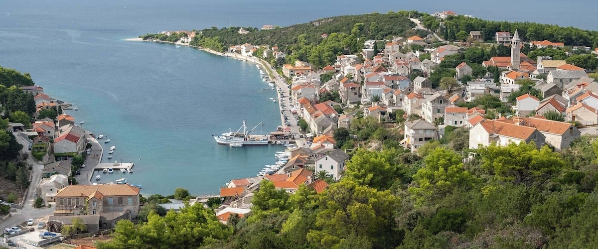 A coastal town with a marina, surrounded by hills and a clear view of the sea.