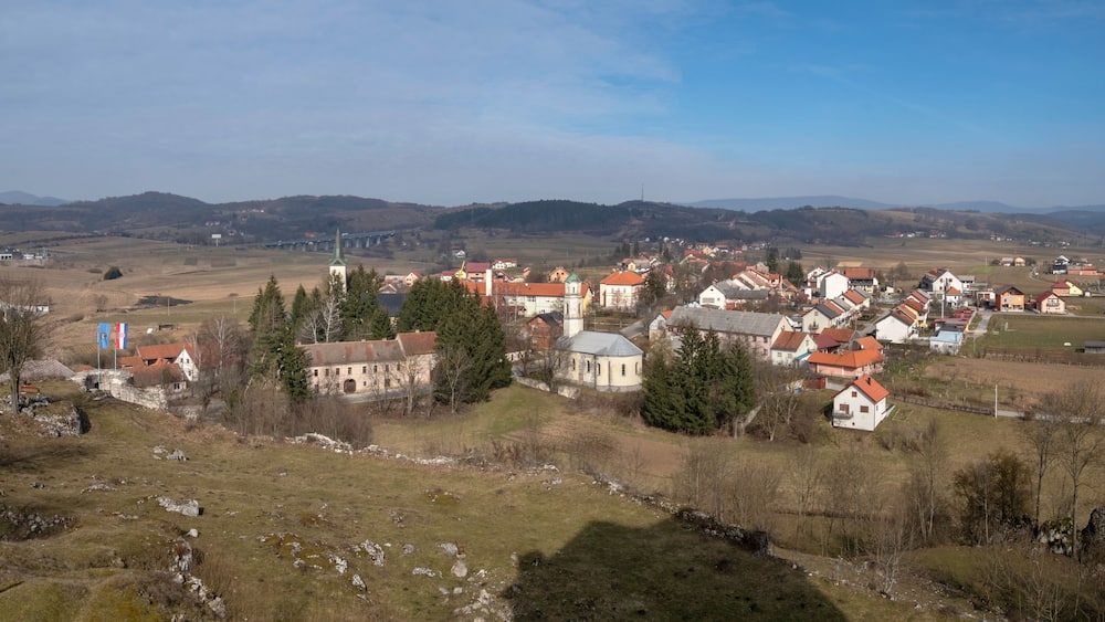 Ein Dorf mit roten Häusern, einer Kirche und einer Brücke im Hintergrund.