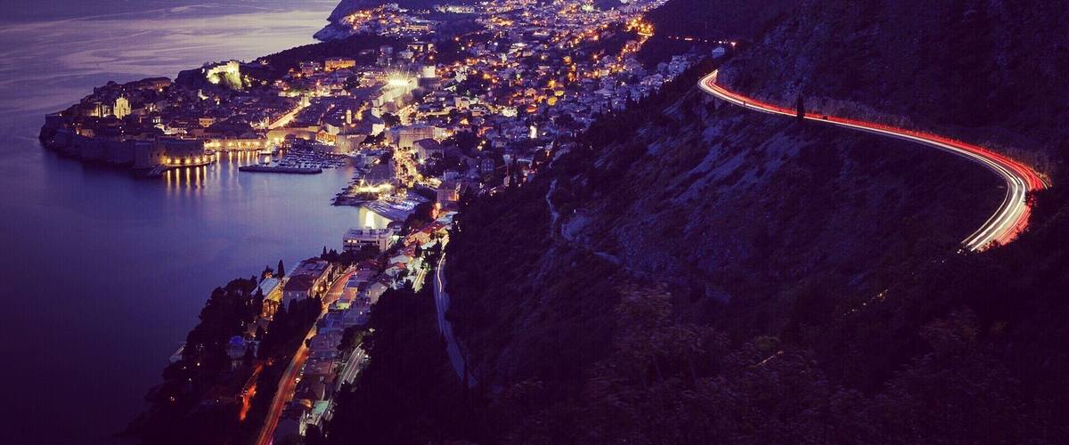 A coastal city at dusk with a winding road along a steep hillside.