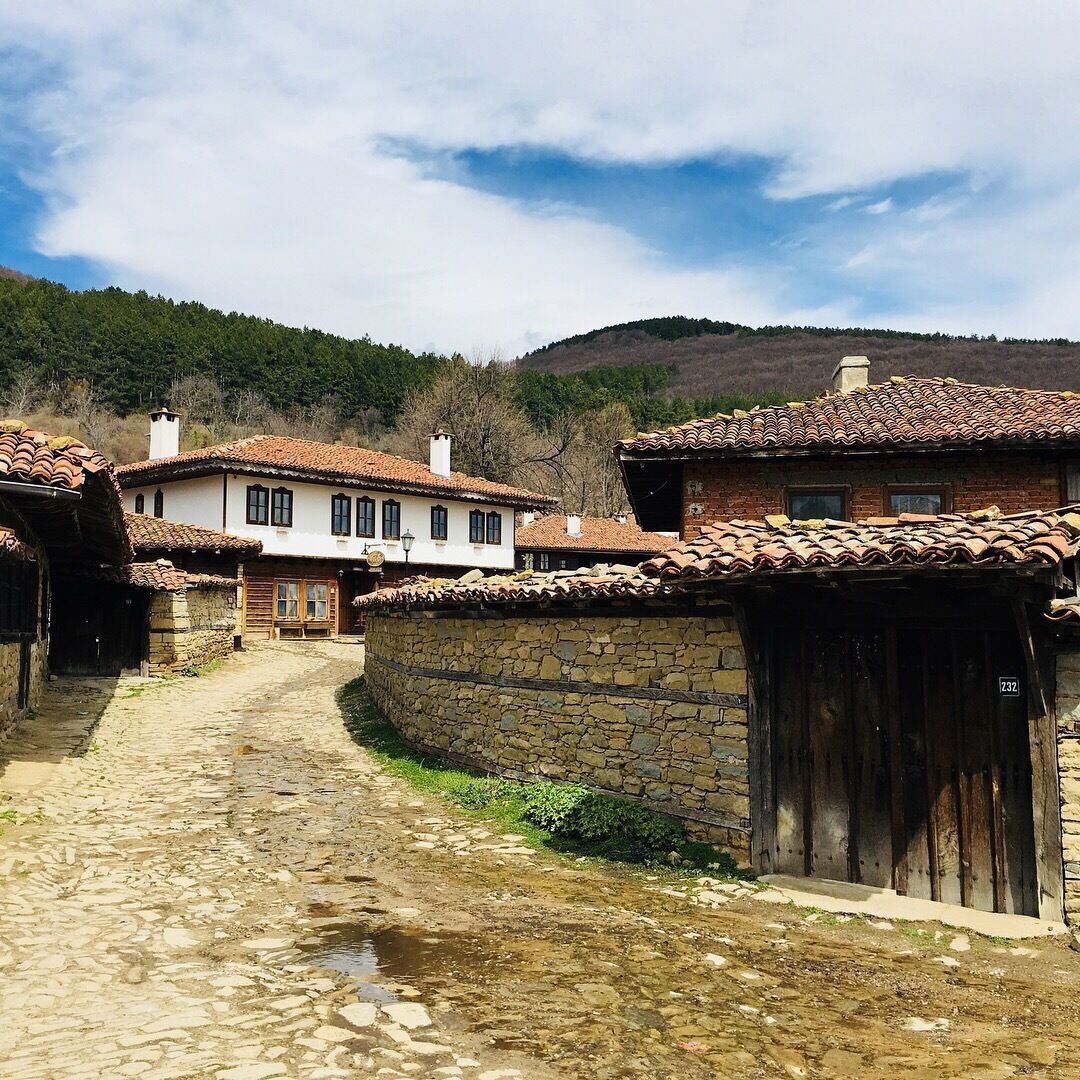 A cobblestone street in a rural village with traditional houses and a stone wall.