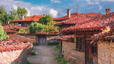 A cobblestone street lined with traditional stone houses with red-tiled roofs.