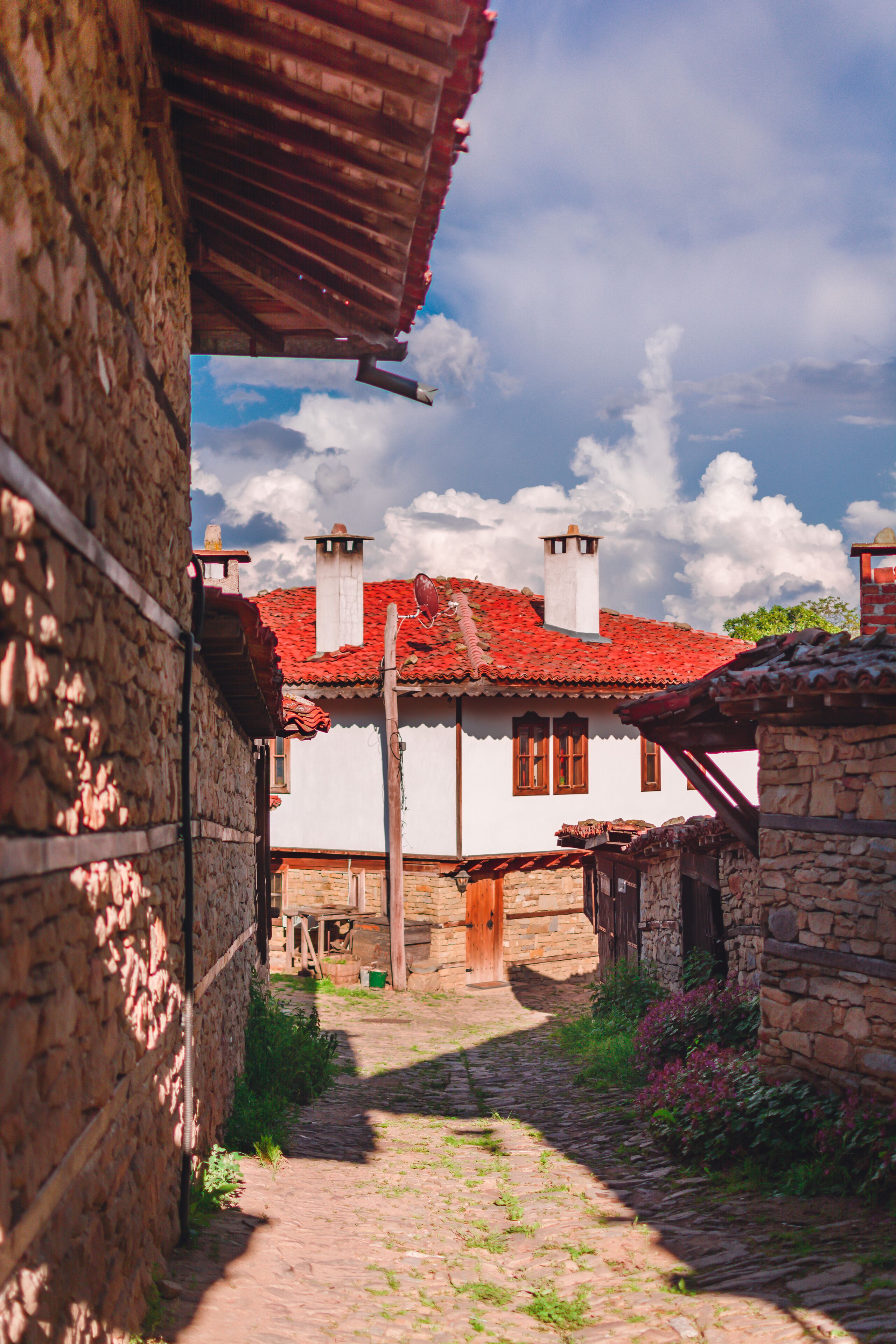 A cobblestone path leading to a traditional white house with a red-tiled roof and stone walls.
