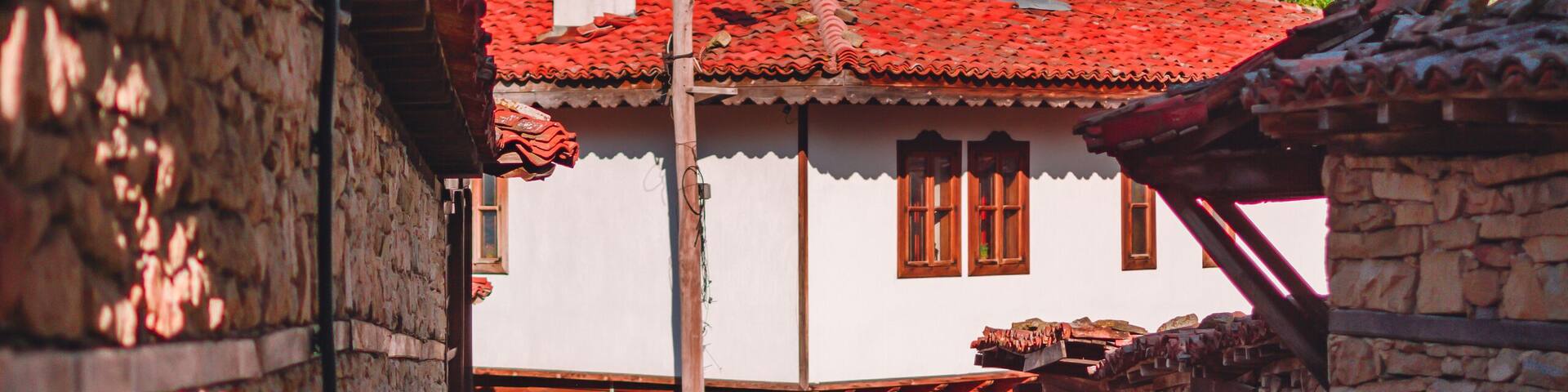 A cobblestone path leading to a traditional white house with a red-tiled roof and stone walls.