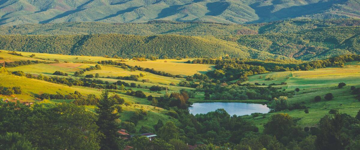 A mountainous landscape with a lake and rolling green fields.
