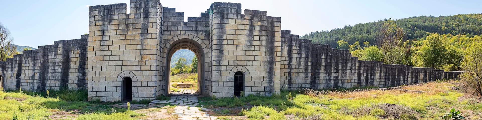 A stone archway leading into a forested area with a mountain in the background.