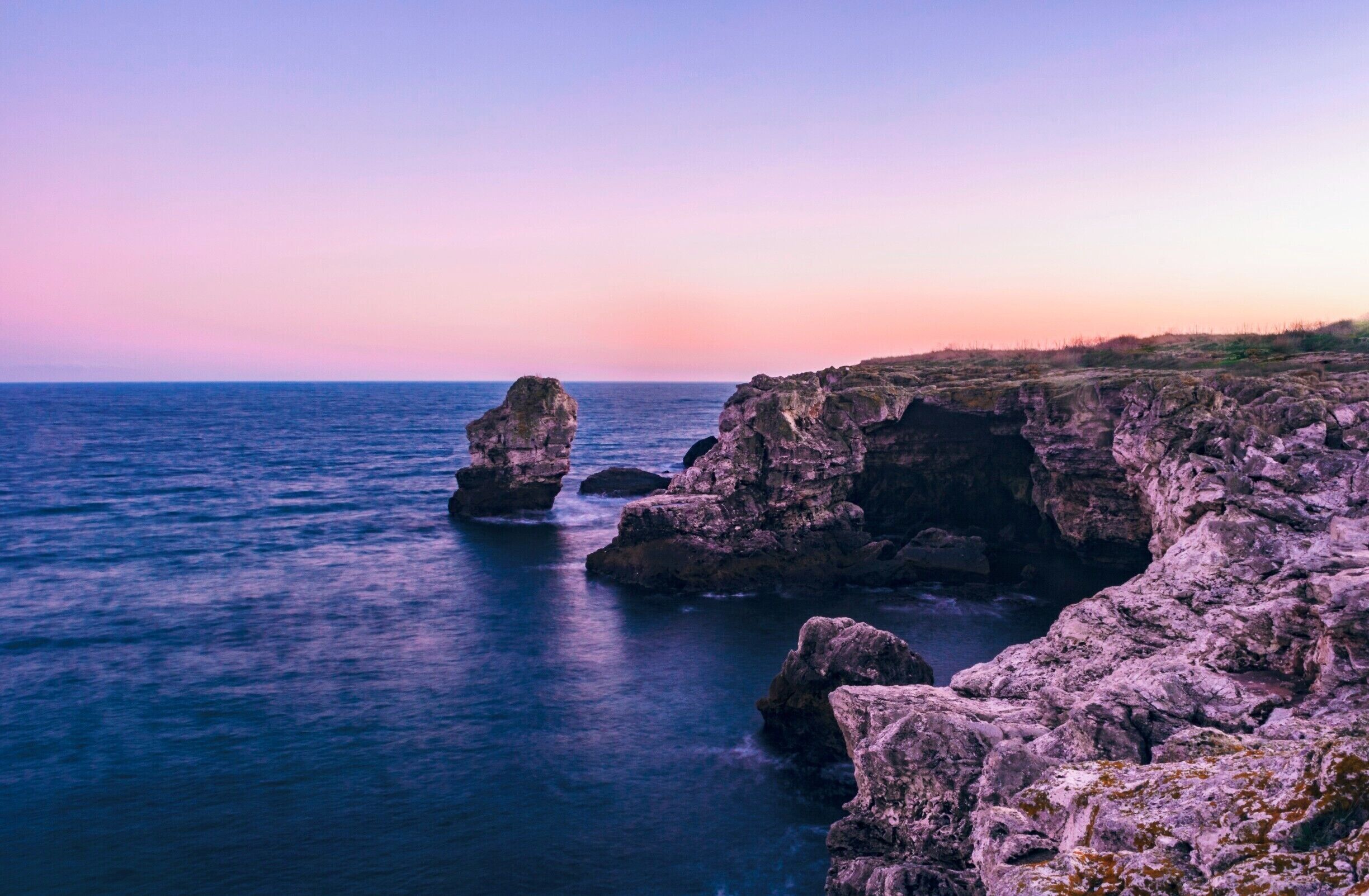 A coastal landscape with rocky formations and calm sea at sunset.
