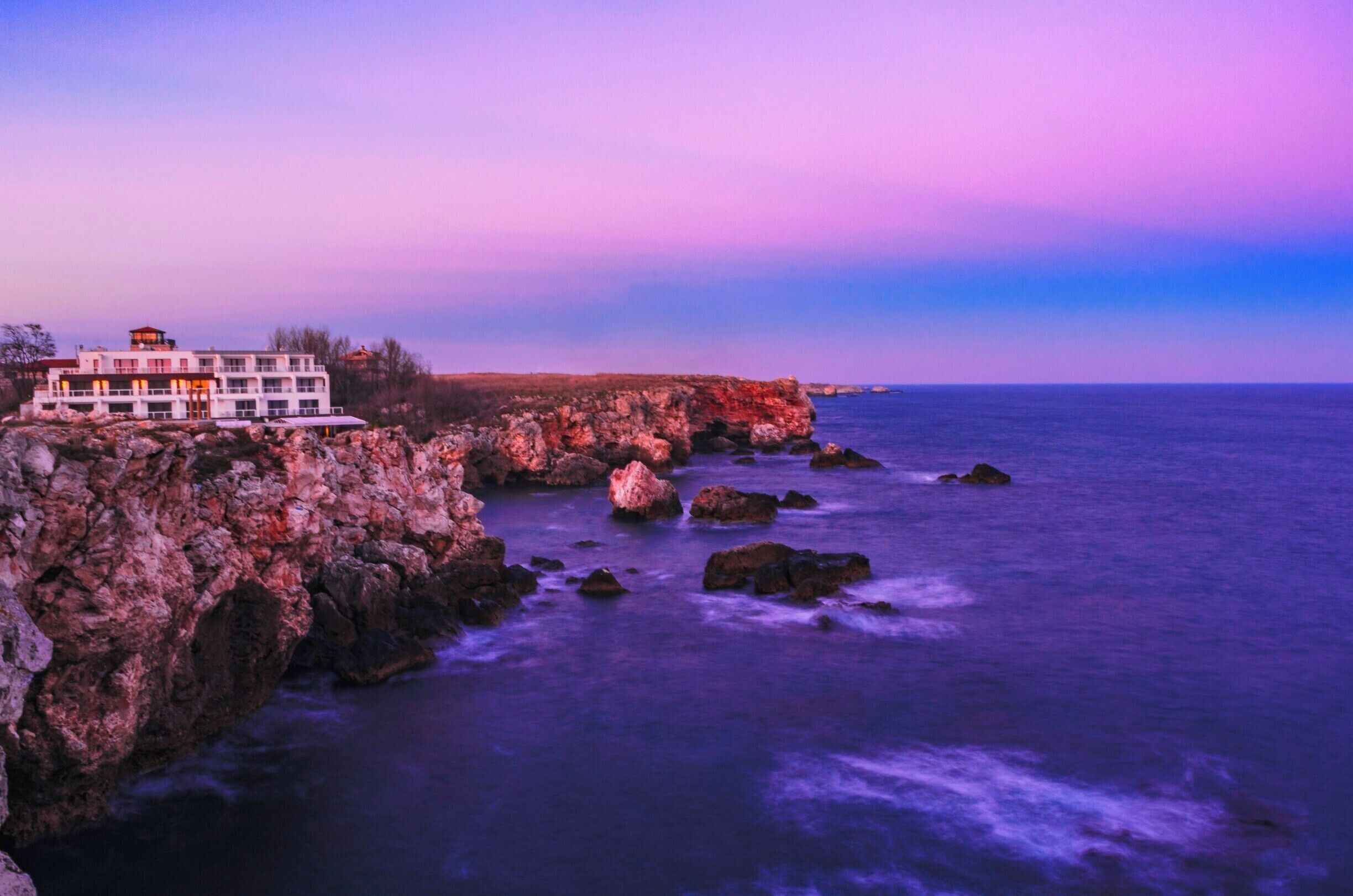 A coastal building on rocky cliffs overlooking the ocean.