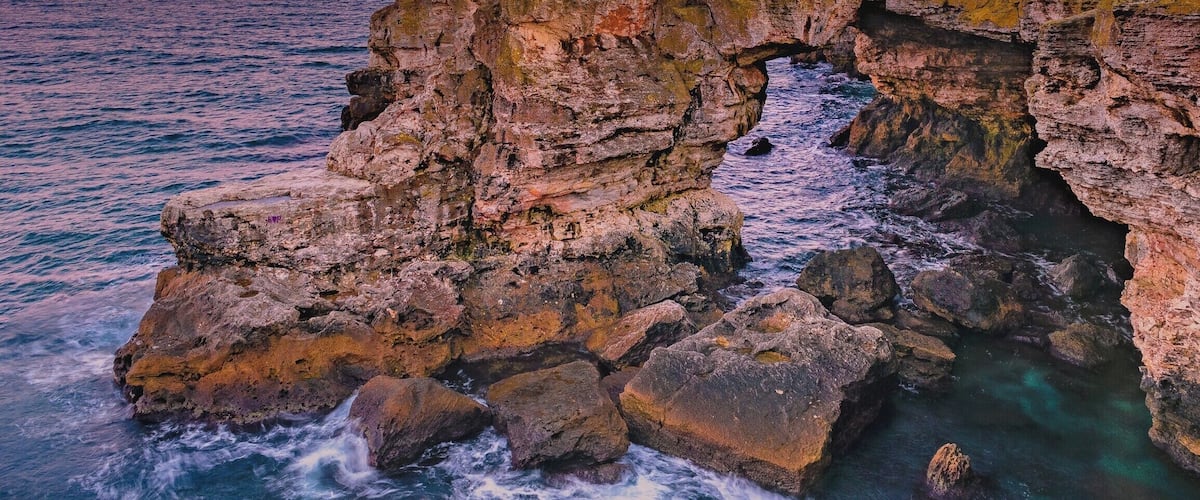 A coastal landscape with a rocky arch formation and the ocean.