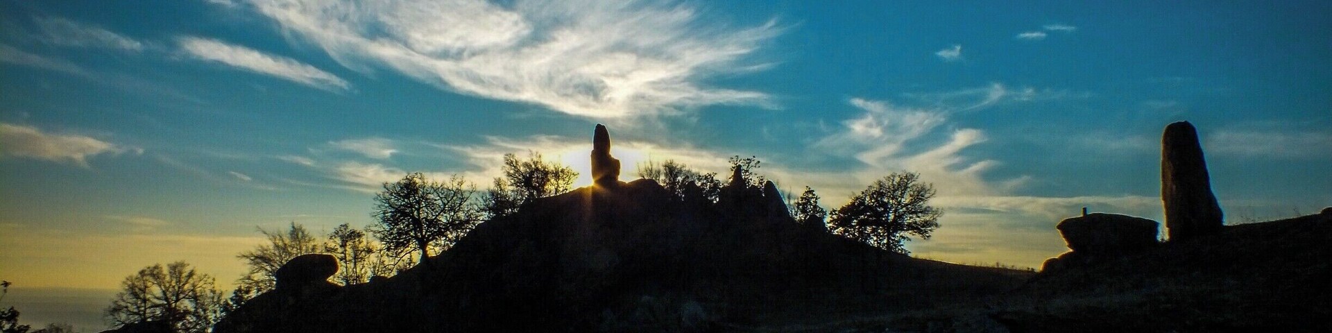 Um pôr do sol sobre uma paisagem rochosa com duas formações de pedra imponentes em silhueta contra o céu.