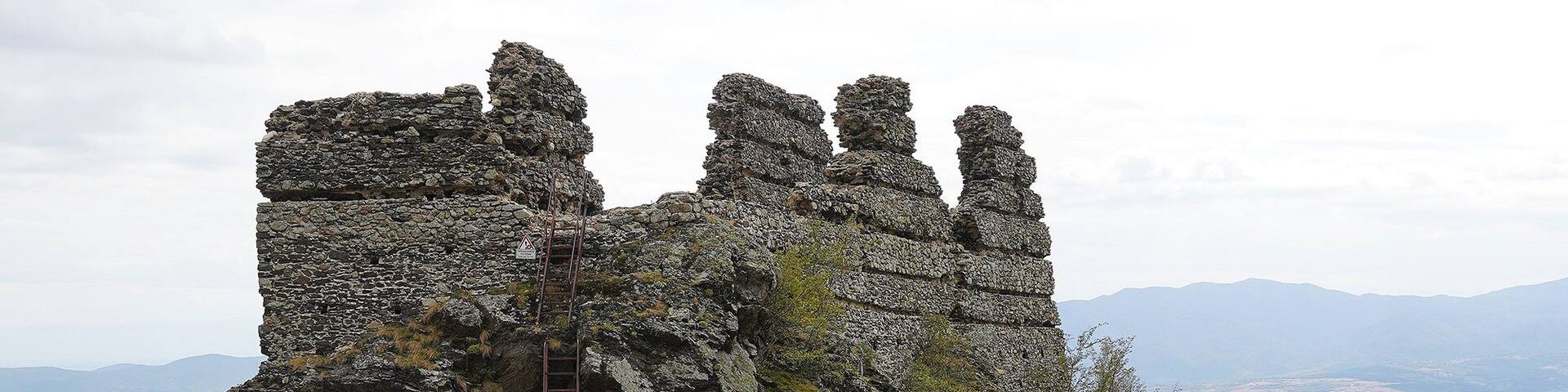 A stone ruin with a ladder leading up, surrounded by rocky terrain and sparse vegetation.