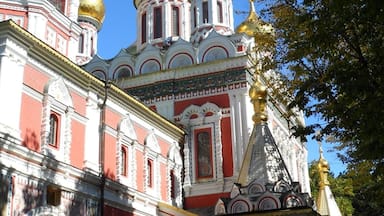 Uma igreja histórica com paredes vermelhas e brancas, cúpulas douradas e uma torre alta.