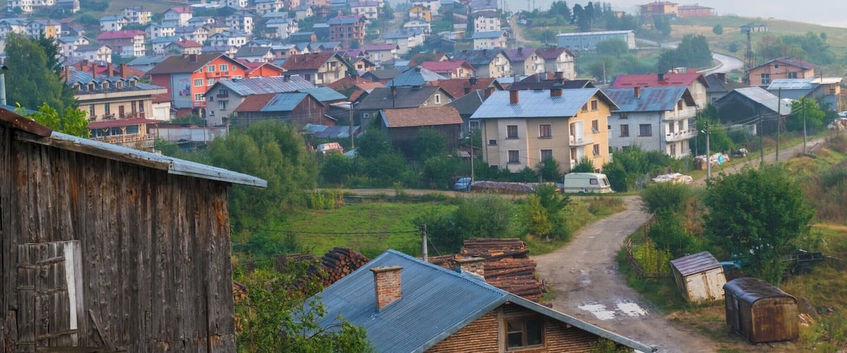 A village with colorful houses, a dirt road, and mountains in the background.