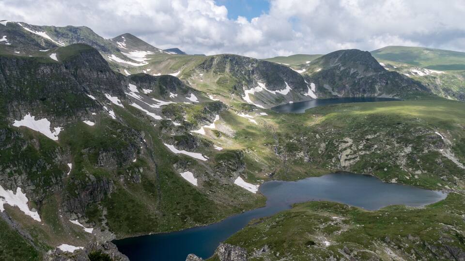A mountainous landscape with a lake surrounded by rocky terrain and patches of snow.