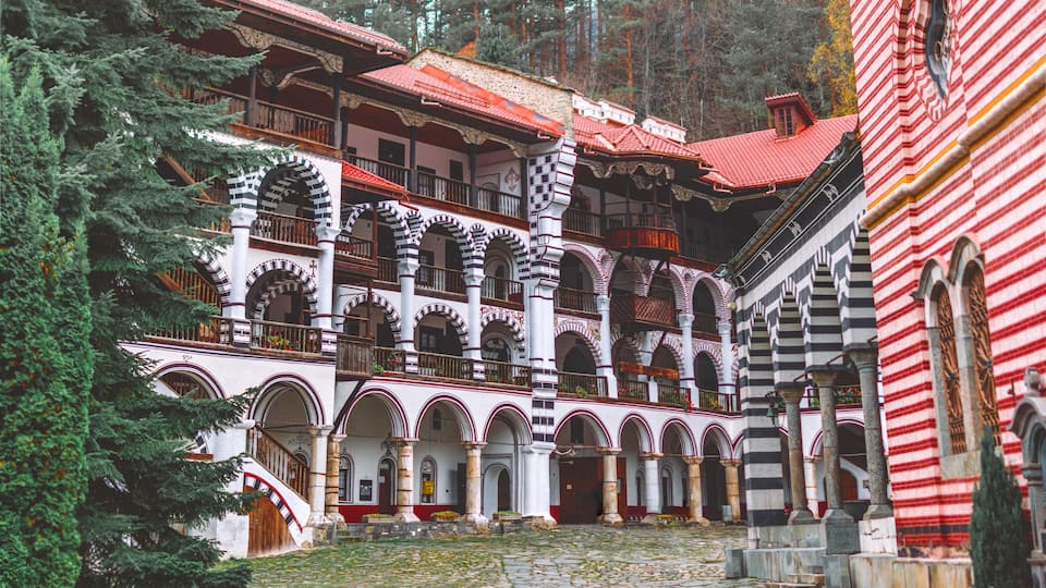 A traditional building with red and white striped walls, surrounded by trees and a cobblestone courtyard.