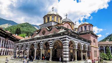 Una iglesia histórica con arquitectura a rayas y cúpulas, rodeada por un patio empedrado y visitantes.