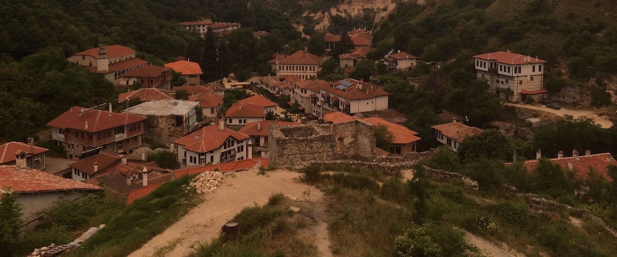 A village nestled in a valley with red-roofed houses and a prominent stone structure.