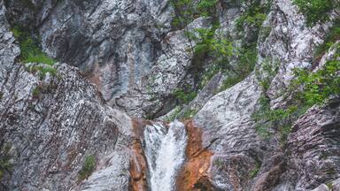A waterfall cascading down a rocky cliff surrounded by greenery.