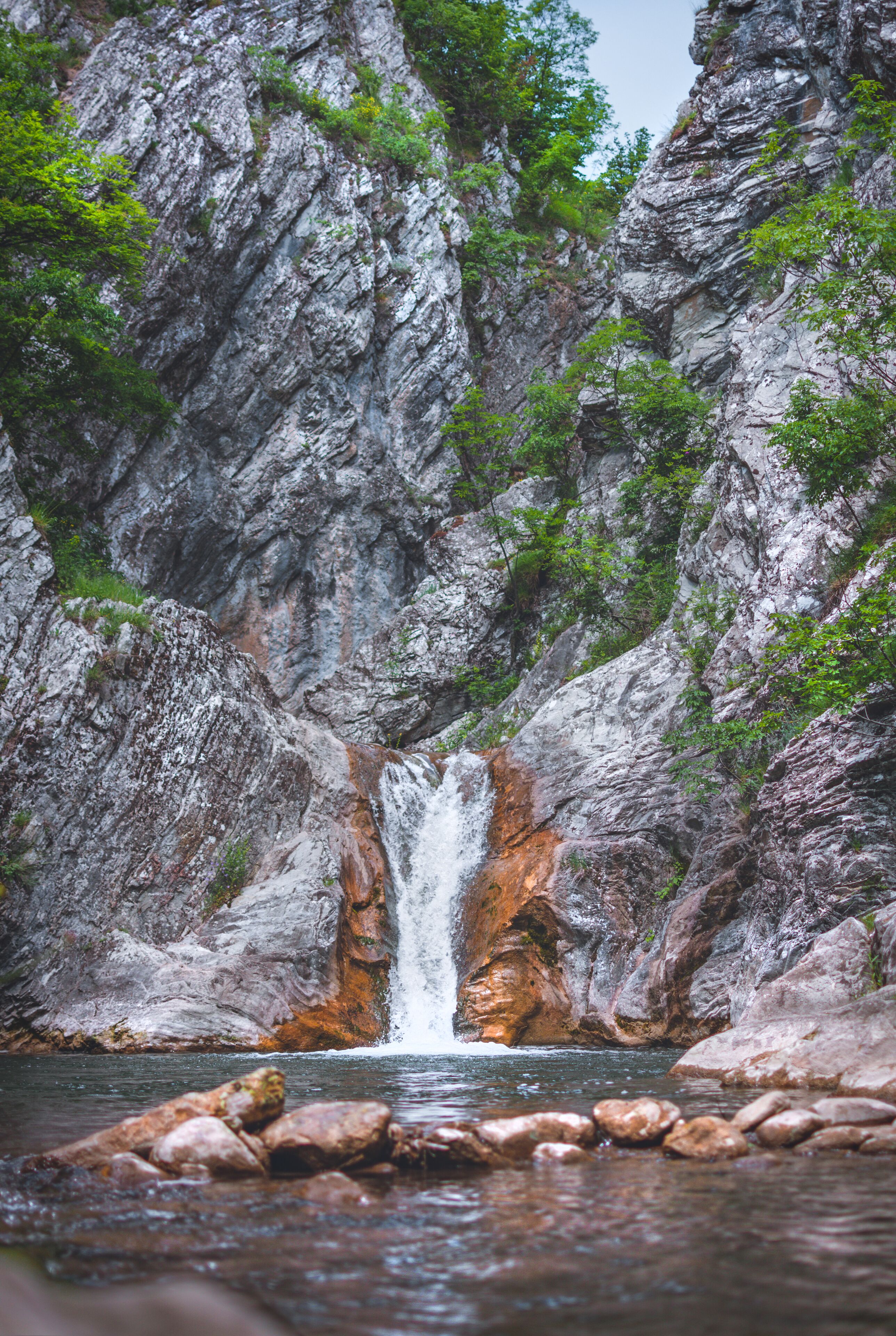 A waterfall cascading down a rocky cliff surrounded by greenery.