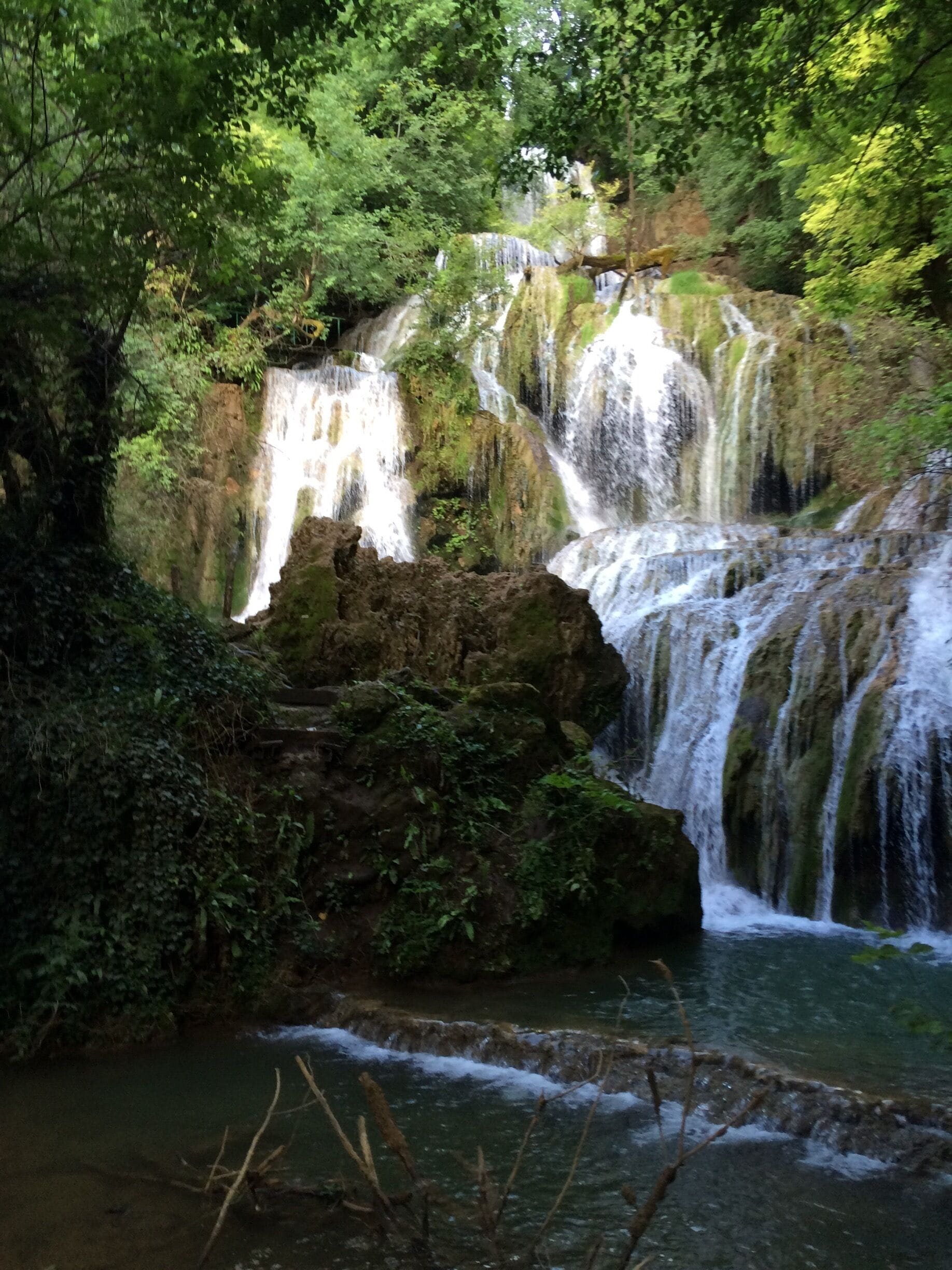 A multi-tiered waterfall surrounded by lush greenery.