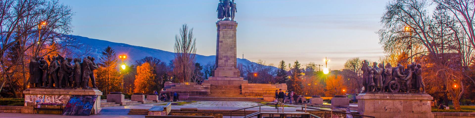 A monument with a statue of people, surrounded by trees and benches in a park.
