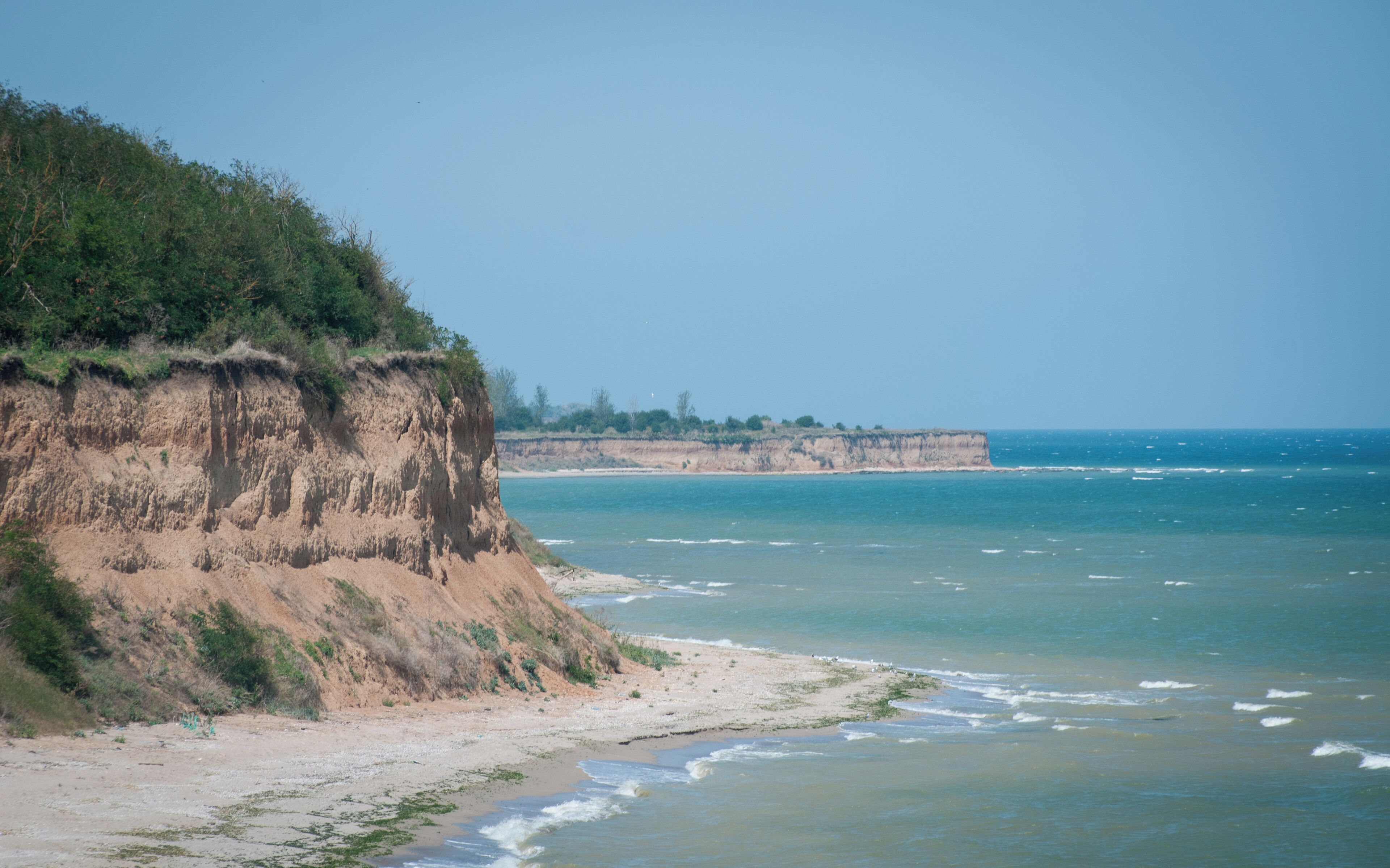 A coastal landscape with a sandy beach, a cliff with sparse vegetation, and a calm sea.