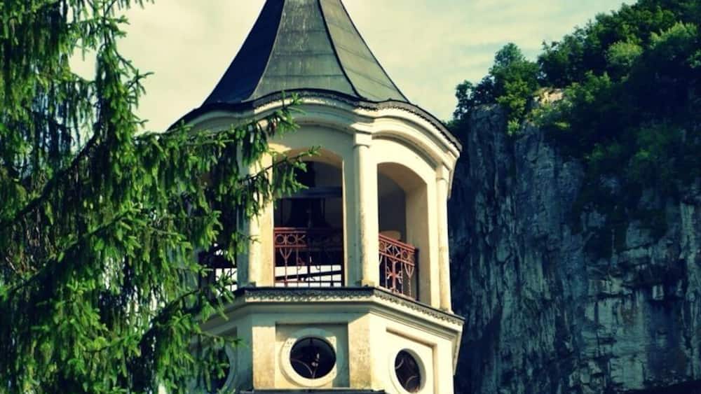 Ein Turm mit spitzer Dachform, einer Uhr und einem Balkon.