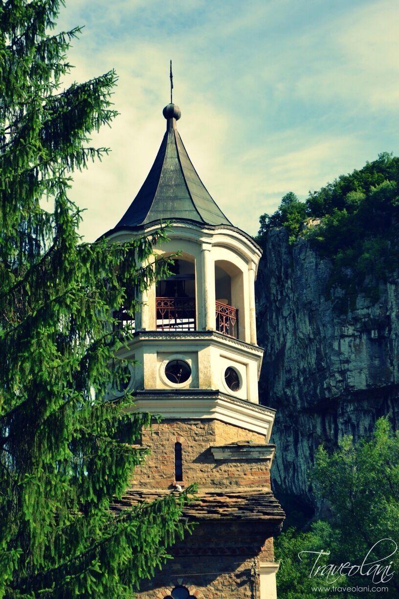 A tower with a pointed roof, a clock, and a balcony.