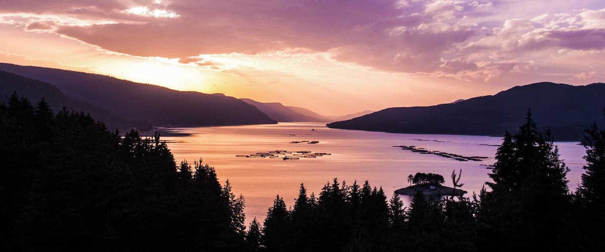 A sunset over a calm lake surrounded by mountains.