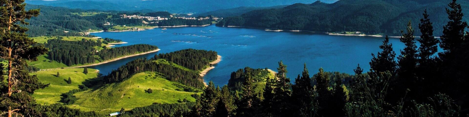 A coastal landscape with a large body of water, surrounded by hills and dense forests.