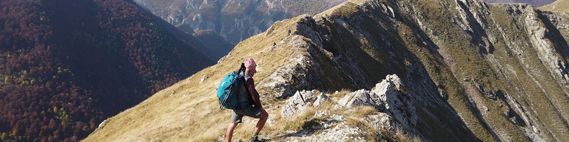 A hiker on a mountain ridge with autumn-colored trees in the valley below.
