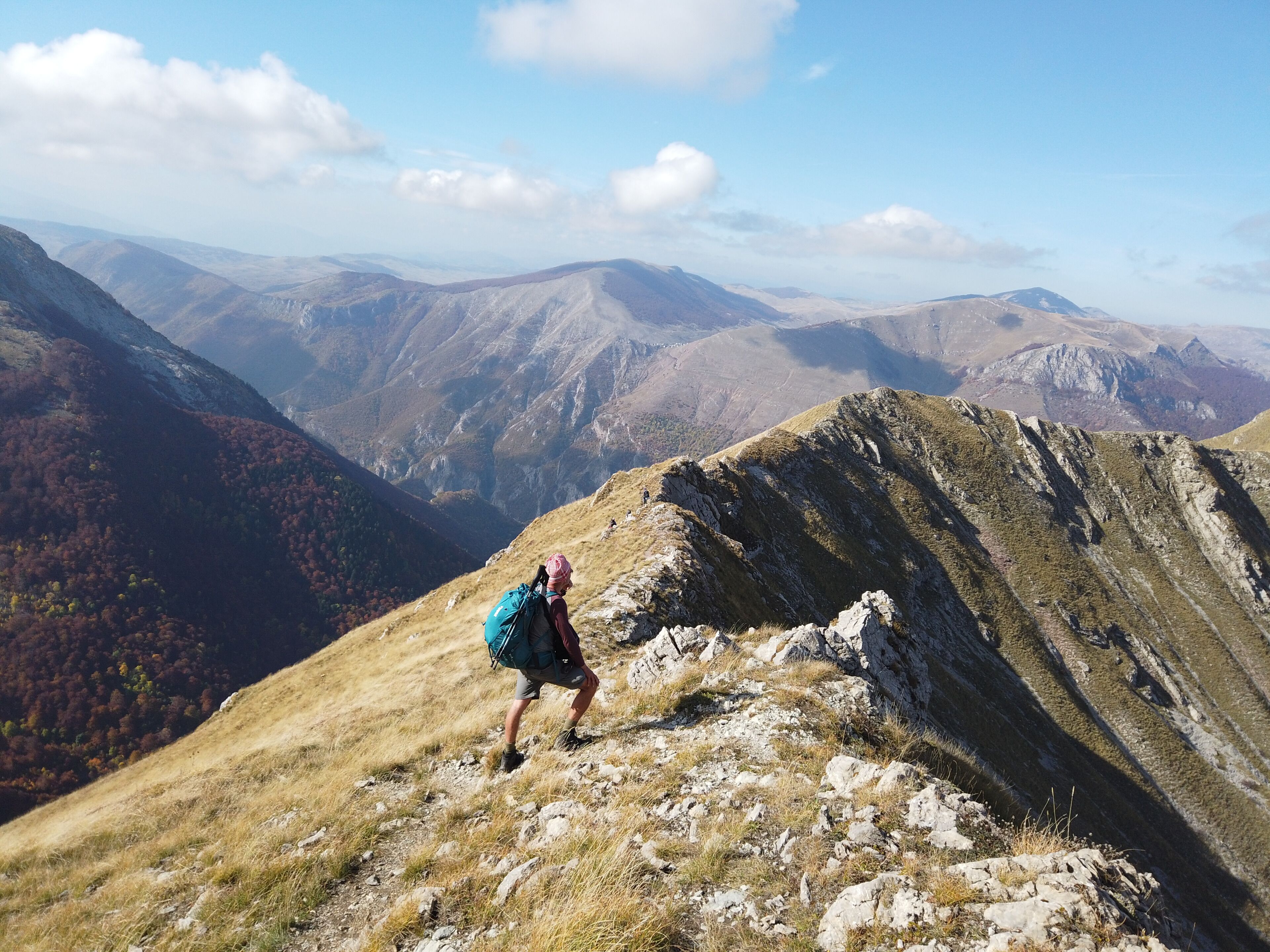 A hiker on a mountain ridge with autumn-colored trees in the valley below.