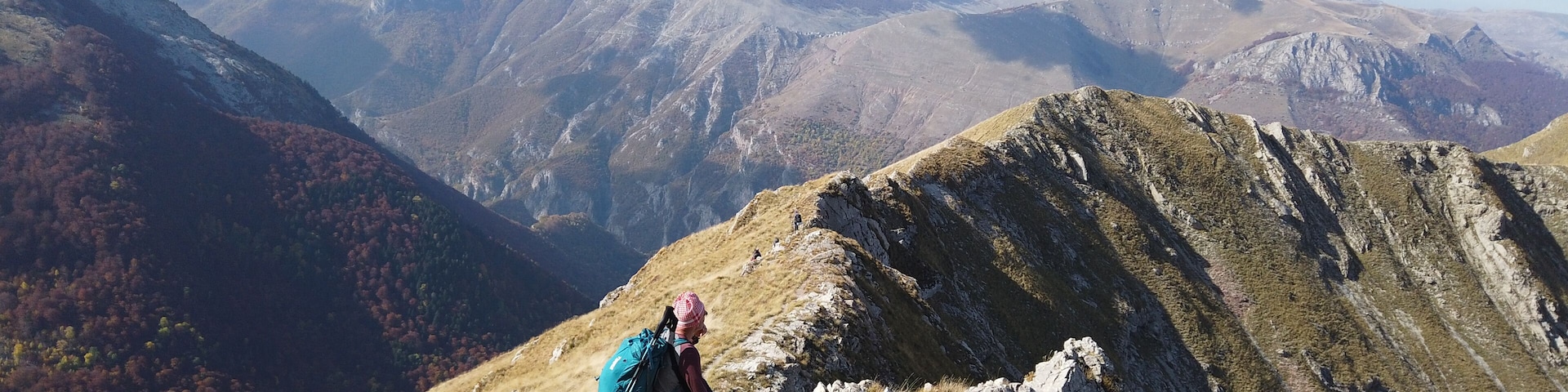 A hiker on a mountain ridge with autumn-colored trees in the valley below.