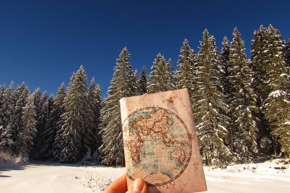 Uma mão segura um mapa, com uma floresta nevada ao fundo.