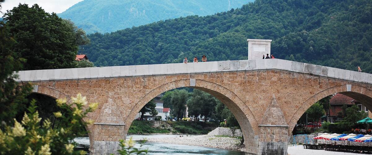 A stone bridge over a river with mountains in the background.
