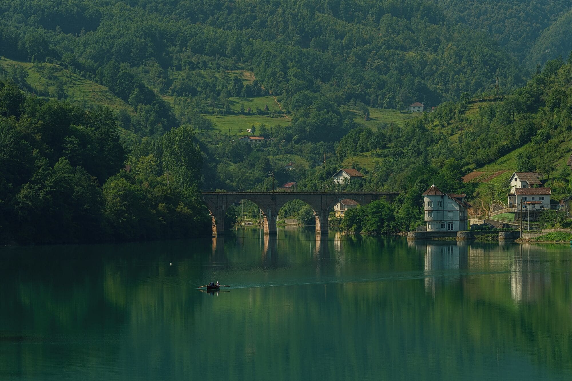 A river with a bridge, surrounded by lush green hills and houses.
