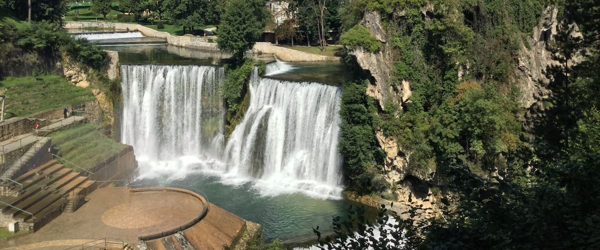 A waterfall cascading down a cliff, surrounded by lush greenery and residential buildings.