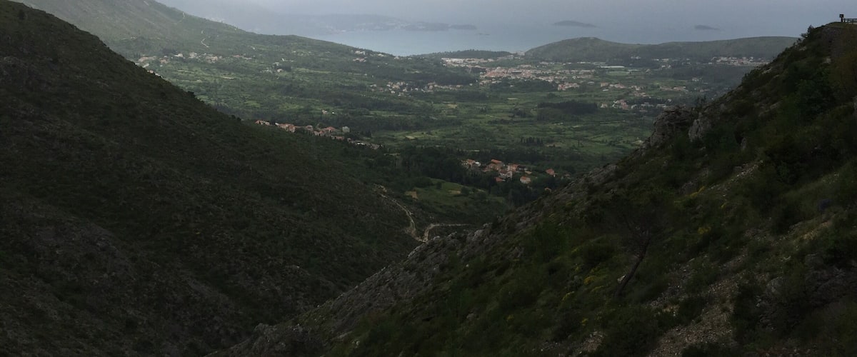 A mountainous landscape with a valley, a winding road, and a distant view of a town.