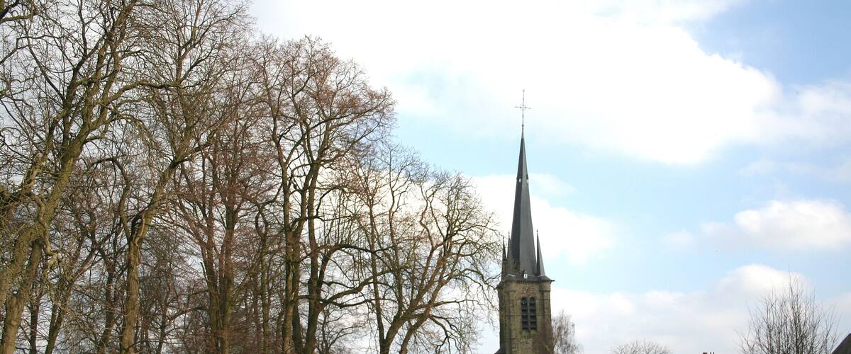 A church with a tall spire, surrounded by trees and buildings.